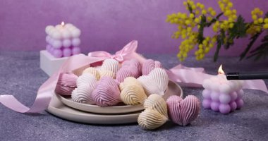 Kalp şeklinde kurabiyeler, mimoza çiçekleri ve mor bir soya baloncuğu mumunu çakmakla yakan bir el ile romantik ve sakin bir ortam yaratıyor.