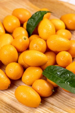 Taze toplanmış kumkatlar canlı turuncu renkler ve derilerinde su damlacıkları sergiliyorlar, yeşil yapraklar sergiliyorlar ve açık ahşap arka planda dinleniyorlar, sağlıklı beslenme kavramları için ideal.