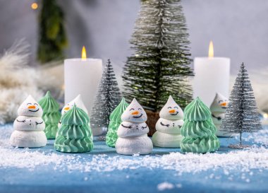 Şirin kardan adam ve Noel ağacı, yanan mumlar ve dekoratif köknar ağaçları ile karlı mavi bir yüzeyde duran tatlı ve şenlikli bir kış tatili sahnesi yaratıyor.