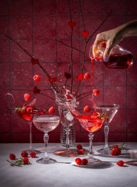 Kadın eli kırmızı kokteyli ahudududulu klasik bardaklara dolduruyor. Romantik, şenlikli bir kutlama sahnesi yaratıyor. Ve zarif sevgililer günü içkileri.