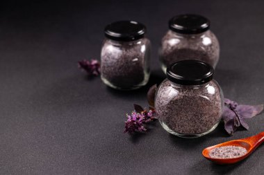 Koyu arkaplanda ev yapımı mor fesleğen tuzu ile dolu üç cam kavanoz ve mis kokulu mutfak çeşnisi ve taze mor fesleğen yapraklarının bir kısmını tutan küçük tahta bir kaşık var.