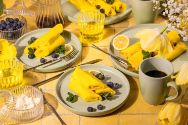 Kahvaltının üstünde yaban mersini ve nane ile sarılmış krep, kahve, limon dilimleri, şurup ve krema ile servis edilen parlak, neşeli bir sabah yemeği.