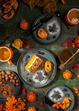 Balkabağı sarmalı, ceviz, tahıl gevreği ve yaban mersiniyle süslenmiş bir balkabağı sarması ve yanında bal, fındık ve ek dekoratif düşme elementleri içeren güz masası seti.