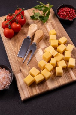 Tahta bir kesim tahtasına yerleştirilmiş peynirin yanında sarmaşıkta taze vişneli domates, pembe tuz, kırmızı biber ve maydanoz.