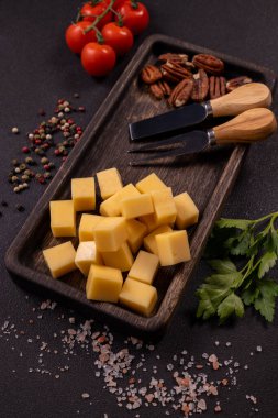 Koyu renkte ahşap bir tepside küp peyniri sunan aperatif tabağında cevizler, kiraz domatesleri ve taze otlar hazır.
