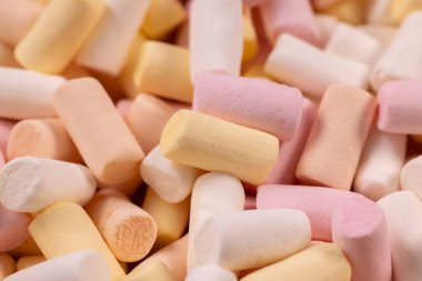 Mini pastel marşmelovlar tatlı, parti ya da sıcak çikolata malzemesi olarak pembe, sarı ve beyaz, kabarık şeker şekerlemelerinin yumuşak ve renkli bir arka planına yığılmıştır.