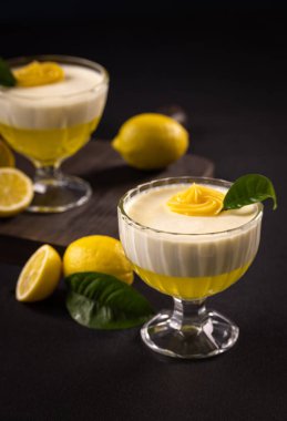 Limon panna cotta ve jöle cam bir kasede ferahlatıcı bir tatlı oluşturuyorlar, krema ve yeşil bir yaprak ile süslenmiş, bütünü ile çevrili ve limon dilimlenmiş