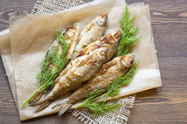 Peixe de rio frito e endro em um papel em um fundo de madeira — Fotografia de Stock