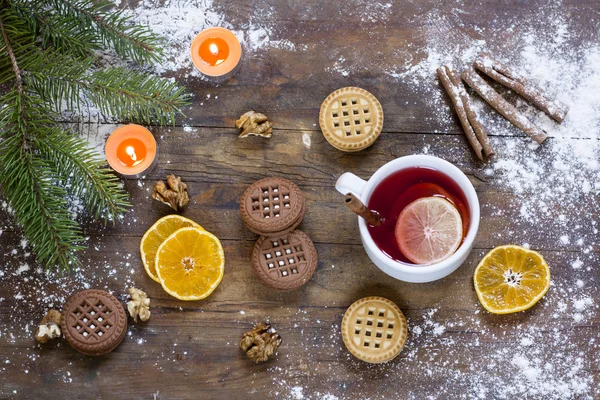 Tea, tangerines and cookies in Christmas decor with Christmas tree, nuts and apples on dark wooden background — Stock Photo, Image