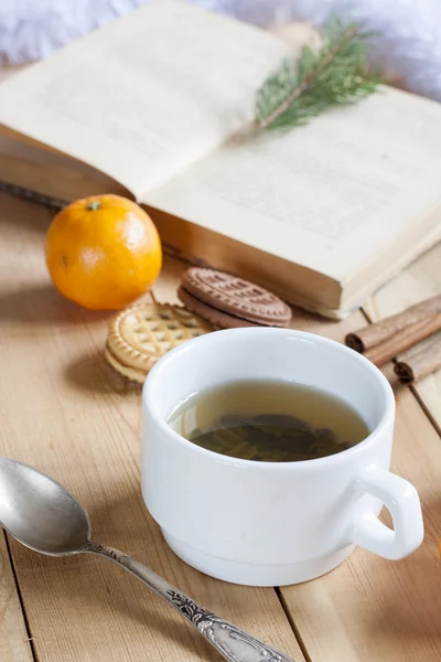 Šálek horkého čaje s knihami, soubory cookie a mandarinky na lehký dřevěný stůl. — Stock fotografie