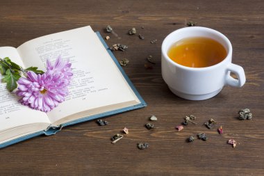 Cup of hot tea with books and flowers and tea leaves