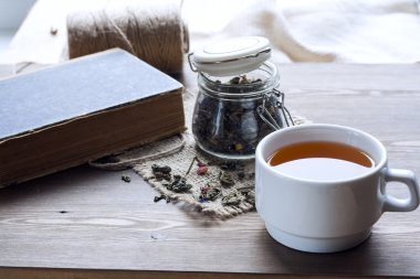 Cup of hot tea with books, tea leaves and flowers on wooden table. Vintage still life.