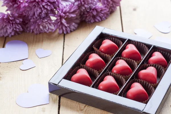 Red chocolate hearts in box and flowers on wooden table