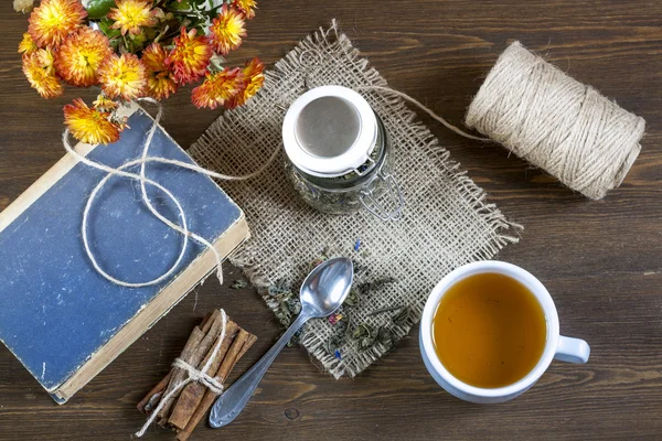 Cup of hot tea with books, tea leaves and flowers on wooden table. Vintage still life. — Stock Photo, Image