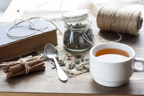 Cup of hot tea with books, tea leaves and flowers on wooden table. Vintage still life. — Stock fotografie