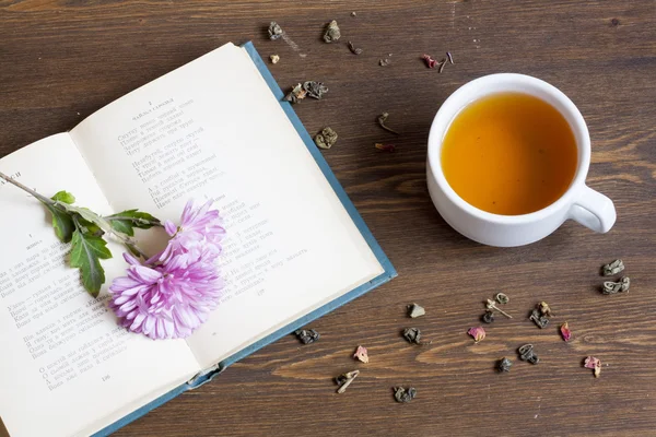Cup of hot tea with books and flowers and tea leaves