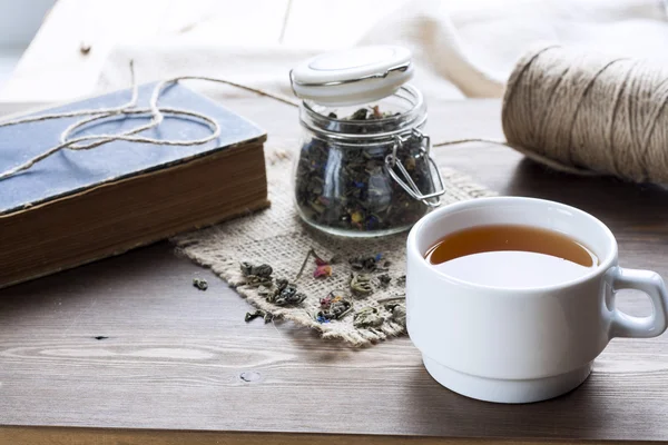 Cup of hot tea with books, tea leaves and flowers on wooden table. Vintage still life. — Stock fotografie