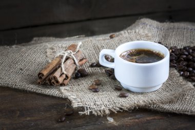 Coffee cup, cinnamon and coffee beans on a wooden background.