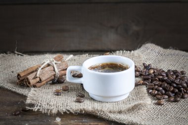 Coffee cup, cinnamon and coffee beans on a wooden background.