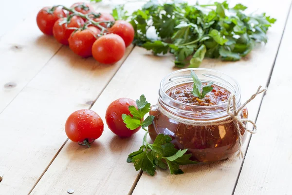 Tomato sauce (jam) in glass jar with parsley and fresh tomatos on dark wooden table, selective focus. — Stock Photo, Image