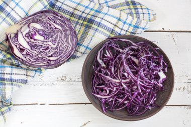Sliced red cabbage in clay bowl on white wooden table