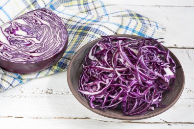 Sliced red cabbage in clay bowl on white wooden table