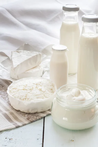 Dairy products. Milk in glass bottle, yogurt, sour milk cheese, sour cream, camembert and brie with checkered napkin on light blue wooden table