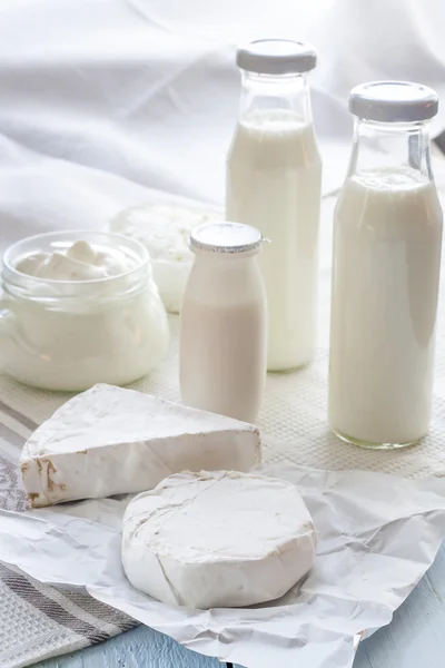 Dairy products. Milk in glass bottle, yogurt, sour milk cheese, sour cream, camembert and brie with checkered napkin on light blue wooden table — 스톡 사진