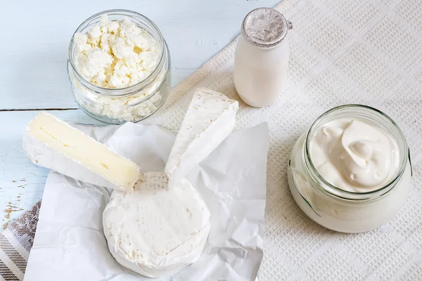 Dairy products. Milk in glass bottle, yogurt, sour milk cheese, sour cream, camembert and brie with checkered napkin on light blue wooden table — Φωτογραφία Αρχείου