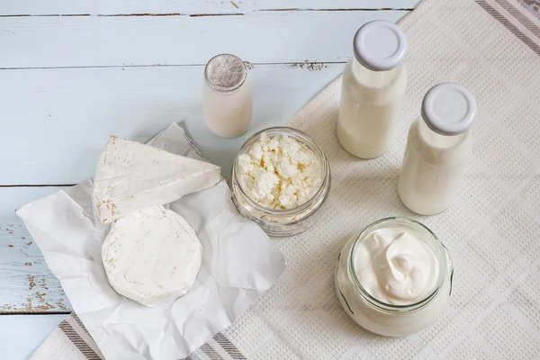 Dairy products. Milk in glass bottle, yogurt, sour milk cheese, sour cream, camembert and brie with checkered napkin on light blue wooden table — Zdjęcie stockowe
