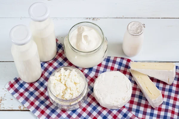 Dairy products. Milk in glass bottle, yogurt, sour milk cheese, sour cream, camembert and brie with checkered napkin on light blue wooden table — Φωτογραφία Αρχείου