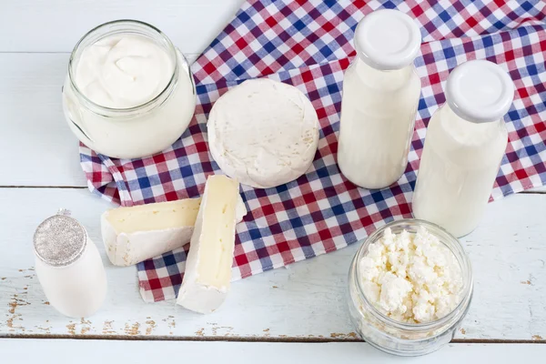 Dairy products. Milk in glass bottle, yogurt, sour milk cheese, sour cream, camembert and brie with checkered napkin on light blue wooden table — ストック写真