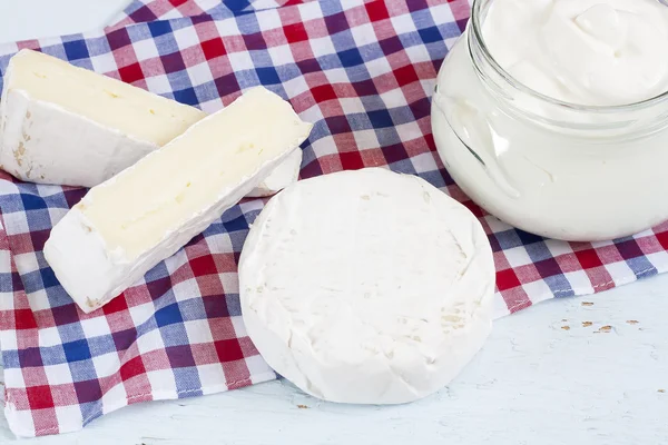 Productos lácteos. Crema agria, camembert y brie con servilleta a cuadros sobre mesa de madera azul claro —  Fotos de Stock