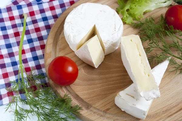 Productos lácteos. Camembert y queso brie con hierbas y tomates sobre tabla de madera —  Fotos de Stock