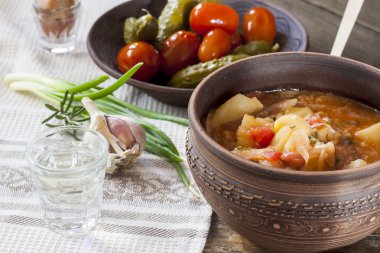 Traditional ukrainian vegetable soup - borsch, marinated tomatoes and cucumbers, sour cream, sliced bread, herbs and garlic at dark wooden table.
