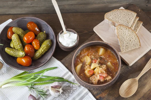 Традиционный украинский овощной суп - борщ, маринованные помидоры и огурцы, сметана, нарезанный хлеб, травы и чеснок за тёмным деревянным столом . — стоковое фото
