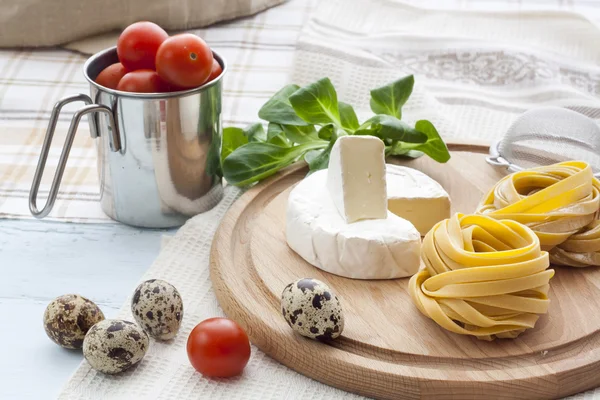 Pasta cruda fatta in casa, uova di quaglia in una tazza di alluminio, lattuga verde, pomodori e farina sul tavolo di legno — Foto Stock