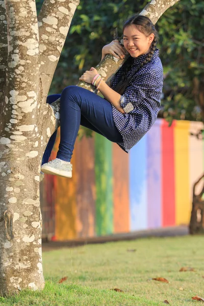 Asian girl playing funny face by climbing on tree branch in publ — Stock Photo, Image