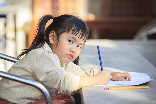 Asiatisk barn med gul blyant i hånd som gjør skolearbeid – stockfoto