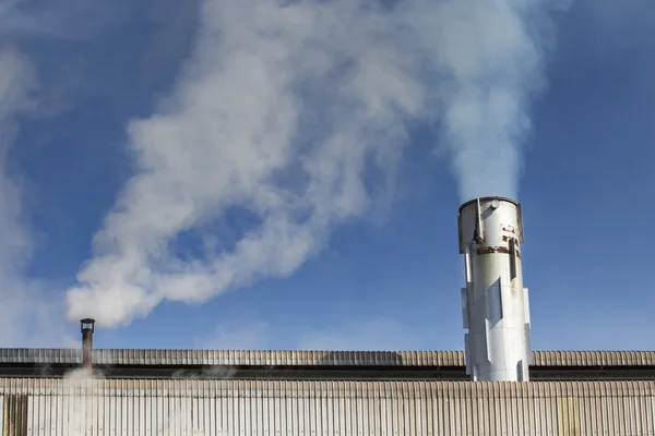Průmyslové mlha z výfukové trubky proti pozadí modré oblohy — Stock fotografie