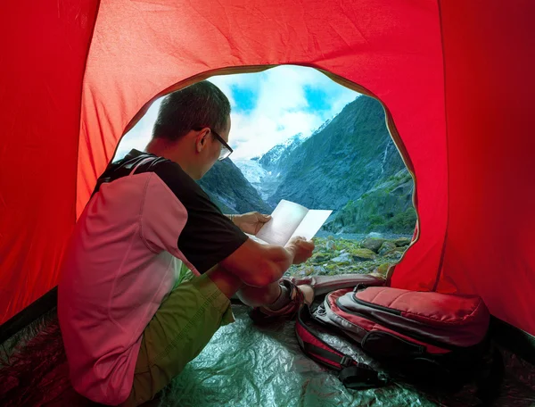 Camping man reading traveling guide book in camp tent against be — Stock Photo, Image