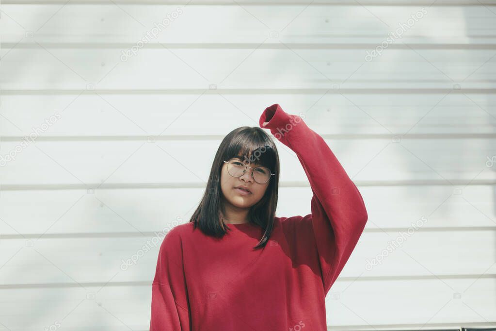 asian teenager wearing red sweater standing against white wall