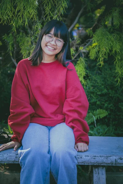 Ahşap masada oturan gözlüklü neşeli Asyalı genç.