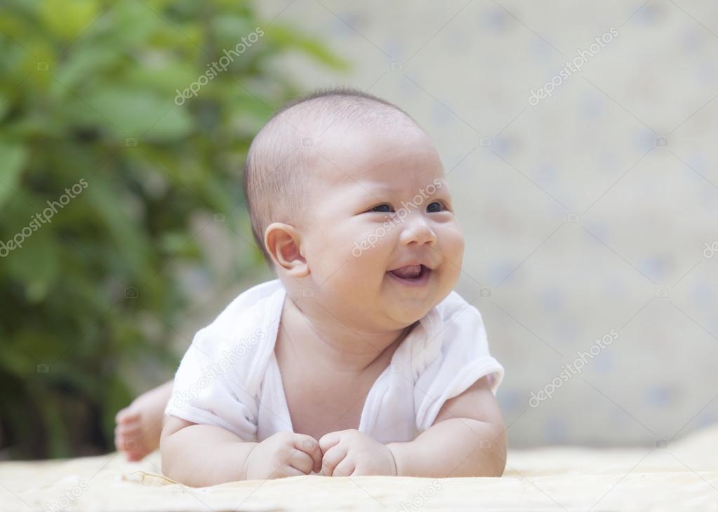 close up face of smiling baby lying on soft bed at home terrace 