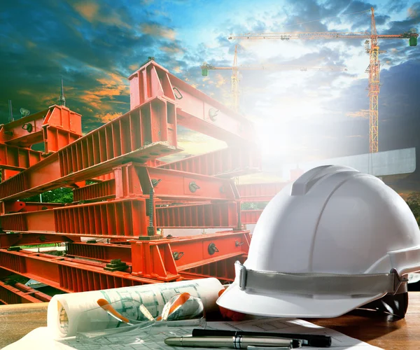 Safety helmet on engineer working table against crane and road c — Stock Photo, Image
