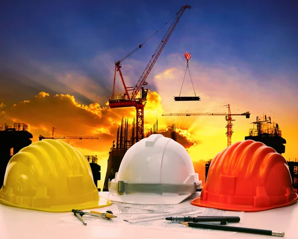 Casco de seguridad en la mesa de trabajo de ingeniero civil contra grúa ascensor — Foto de Stock