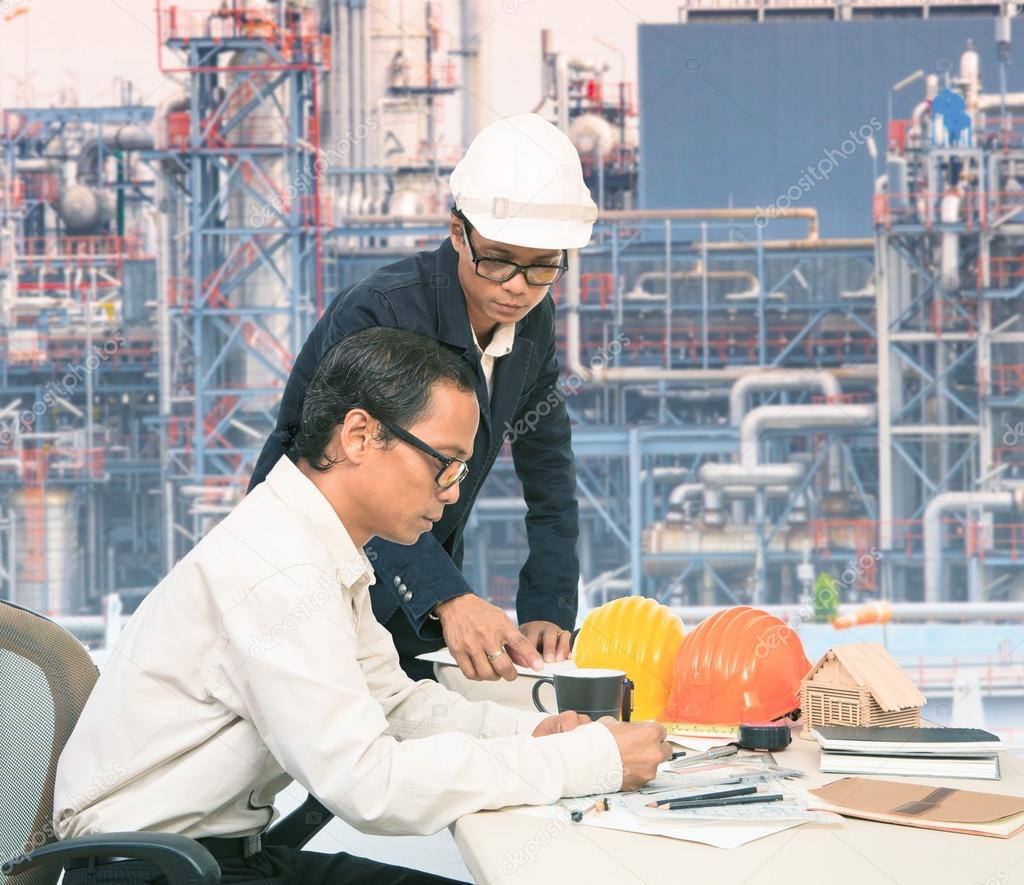 two engineer working on table against exterior of oil refinery p