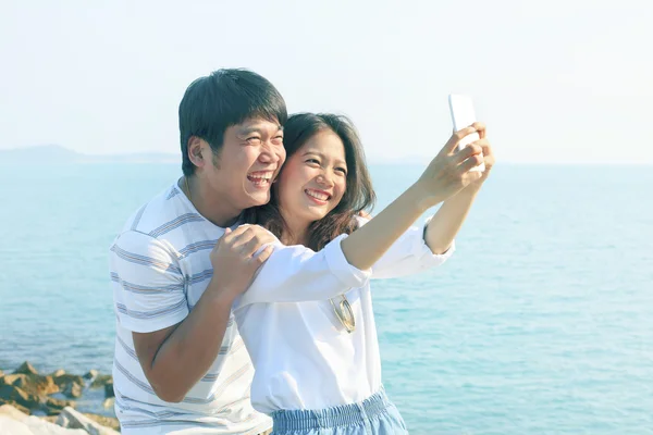 Jonge man en vrouw nemen een foto door slimme telefoon op zee kant gebruik — Stockfoto