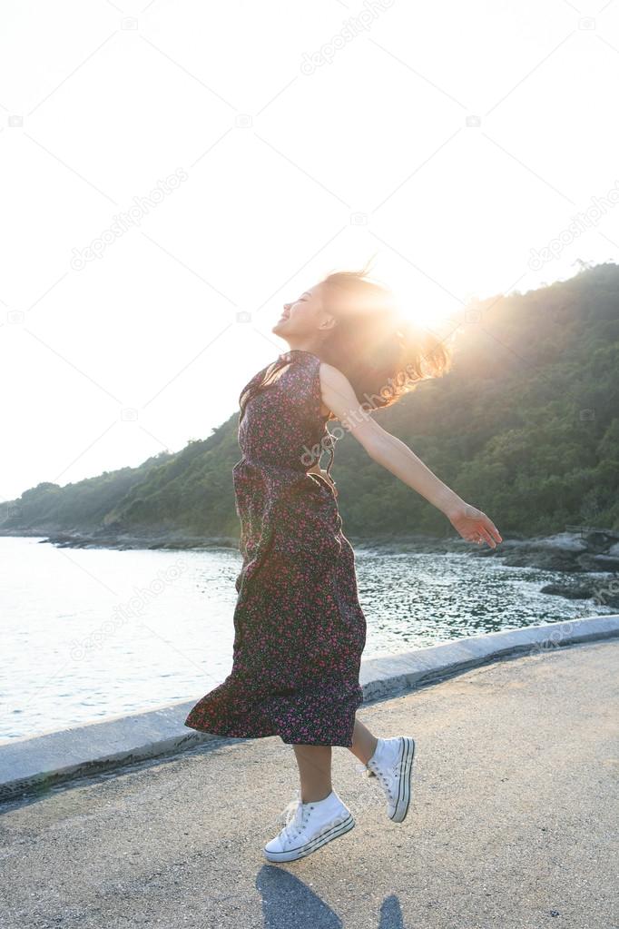 Beautiful young woman jumping at sea side against sun lighting over sky