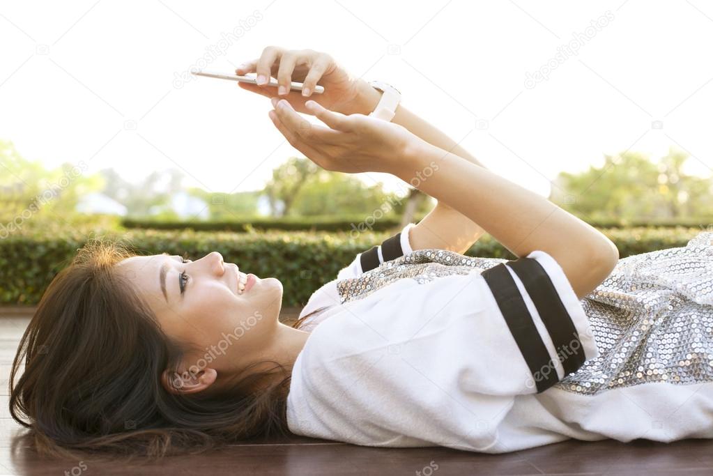 young beautiful woman lying on home terrace and playing smart ph